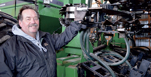 Michel Forget pose devant la machine qui a été modifiée pour faciliter le travail du sol en bande et appliquer l’engrais.