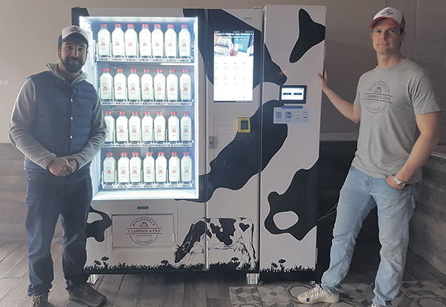 Alexandre Lampron et Guillaume Béland devant la première machine en opération pour la distribution du lait fermier en bouteille. Photo : Gracieuseté de Proxifrigo