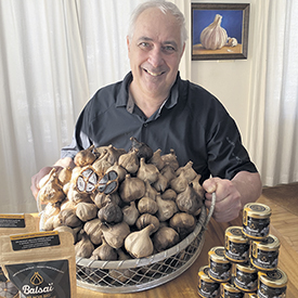 Fondateur et propriétaire de Balsaïl, Robert Duplain pose ici avec un lot de bulbes d’ail noir et de petits contenants de pâte d’ail noir.